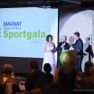 Blick aus dem Publikum auf eine Bühne, auf der drei Menschen vor dem Rednerpult stehen. Die Leinwand hinter ihnen zeigt das goolkids-Logo und die Aufschrift "Magnat-Sportgala".