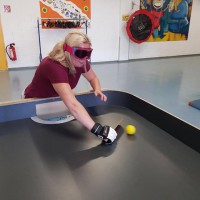 Sportlerin mit Augenbinde mit Handschuh an einem Showdown-Tisch, die gerade einen Ball schlägt